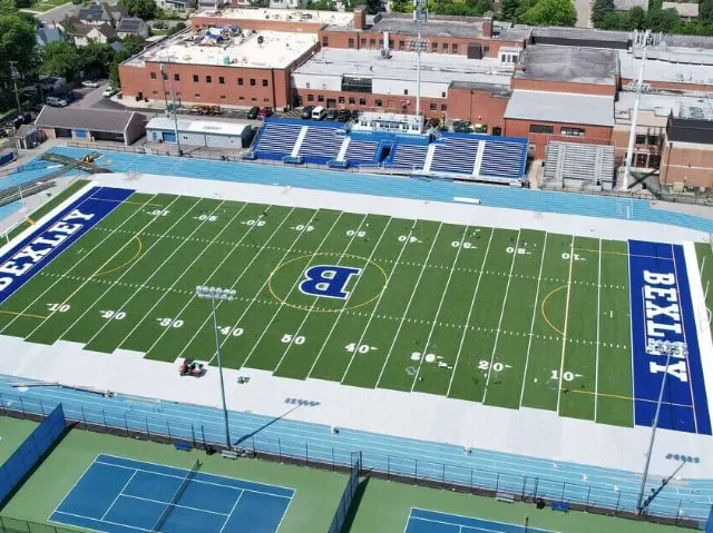 Aerial view of the Bexley stadium with its replaced green turf field, BEXLEY lettering in both end zones and the blue track around it
