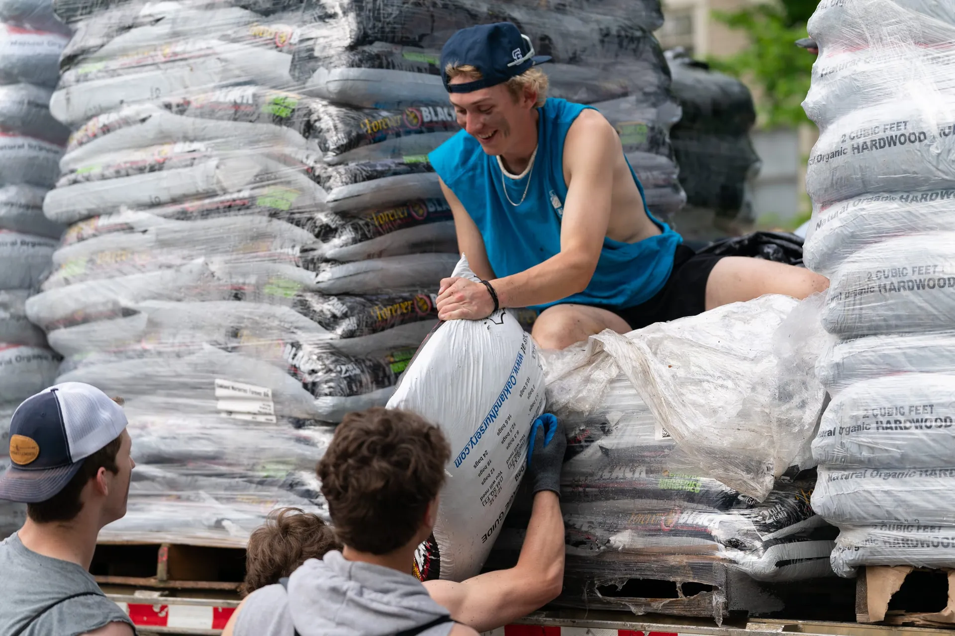 A volunteer atop a pallet-stacked flatbed handing a mulch bag down to the crew during the spring mulch drive
