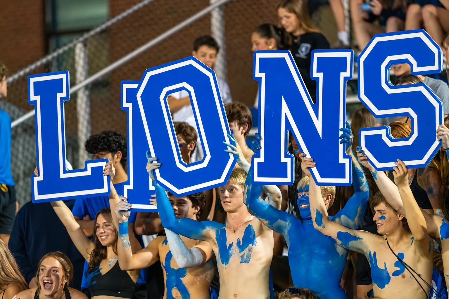 Painted-up Bexley students holding giant letters spelling LIONS in the stands