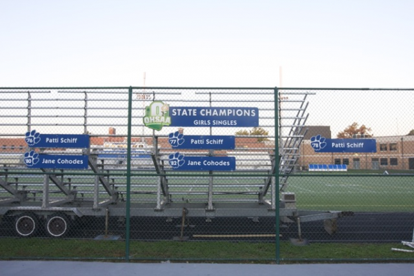 State champions signage bearing the Schiff name along the fence at the rebuilt Bexley tennis courts
